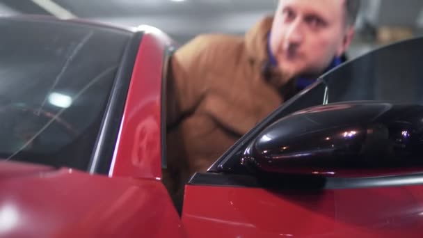 Мужчина садится в красную спортивную машину со стороны водителей. Вид крупным планом — стоковое видео
