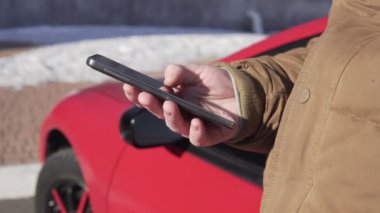 Onun akıllı telefon, arka plan, büyük camları olan bina modern kullanarak arabanın yanında oturan genç adam
