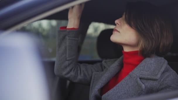 Ділова жінка в сірому пальто і червона черепаха наносить макіяж в машині — стокове відео