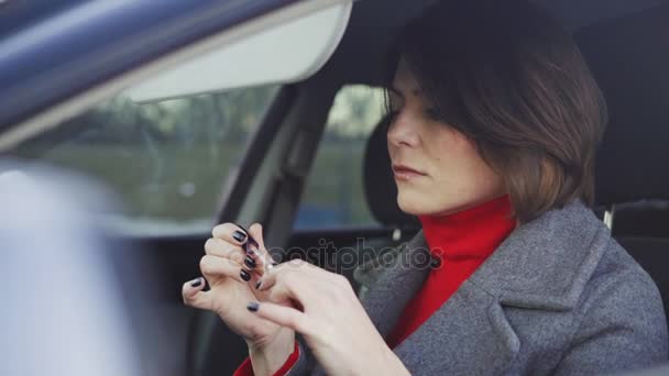 Business woman in grey coat and red turtleneck applying makeup in the car — Stock Video