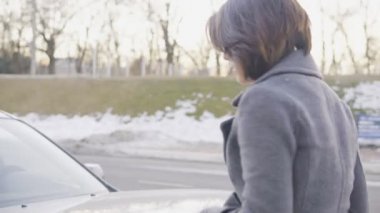 Çekici kadın araba kaput açma ve sokakta başlık altında seyir gri paltolu