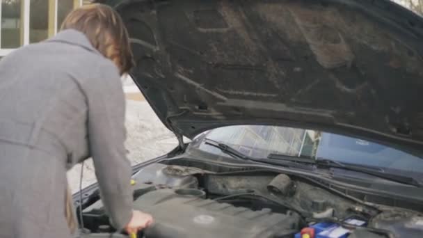 Biznes kobieta sprawdza poziom oleju w samochodzie, patrząc pod maską na ulicy — Wideo stockowe