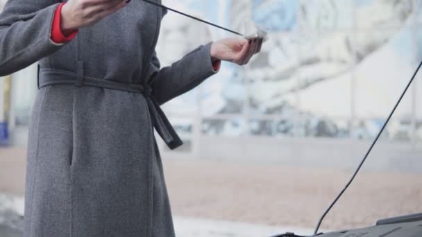 Business woman checks the oil level in the car looking under the hood in the street. Take out the dipstick — Stock Video