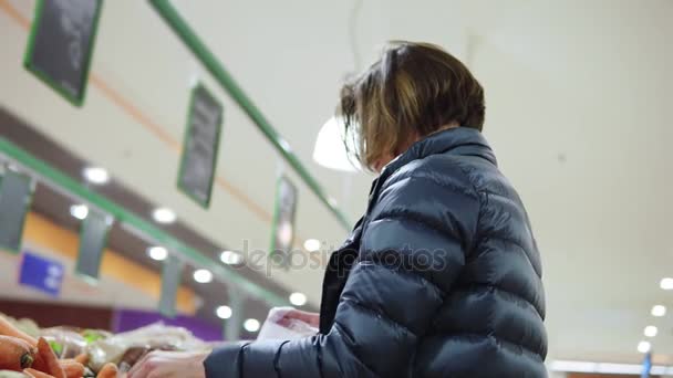 Jonge vrouw winkelen in supermarkt wortelen nemen naar de plastic zak — Stockvideo