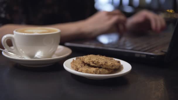 一杯のコーヒーと coockies。バック グラウンドでのラップトップで働く女性 — ストック動画