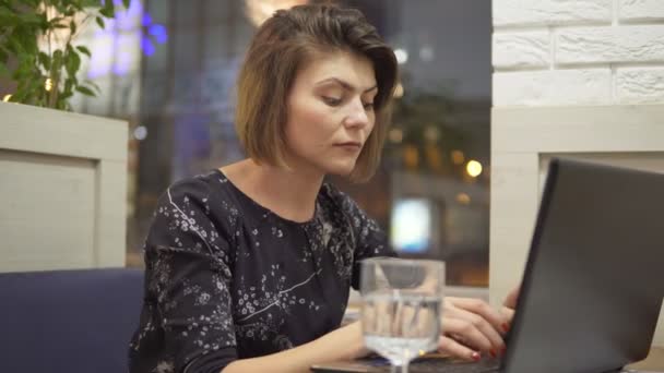 Joven mujer de negocios sentada en un café con un ordenador portátil y trabajando — Vídeo de stock