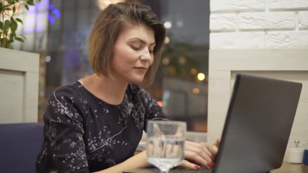 Jonge zakenvrouw zitten in een cafe met een laptop-, arbeids- en drinkwater — Stockvideo