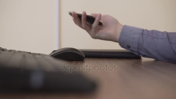 Ruce z poloviny dospělého muže pomocí inteligentního mobilního telefonu sedí u pracovního místa poblíž počítače a klávesnice. — Stock video