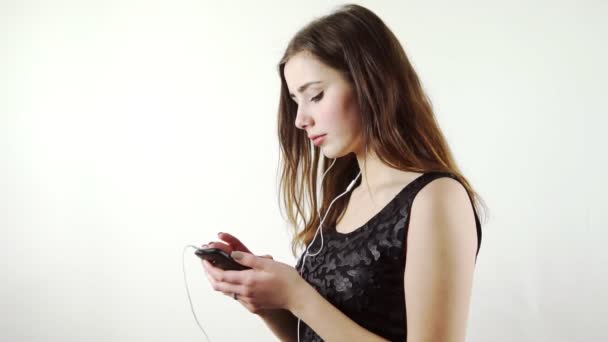 Γυναίκα ακούγοντας τη μουσική από το τηλέφωνο με ακουστικά χορό σε λευκό φόντο — Αρχείο Βίντεο