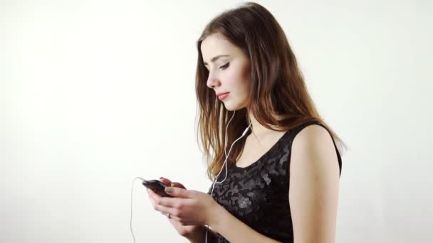 Mujer escuchando la música en su teléfono con auriculares bailando en el fondo blanco — Vídeos de Stock