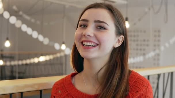 Una joven linda sonríe a la cámara en el fondo de la cafetería de cerca — Vídeo de stock