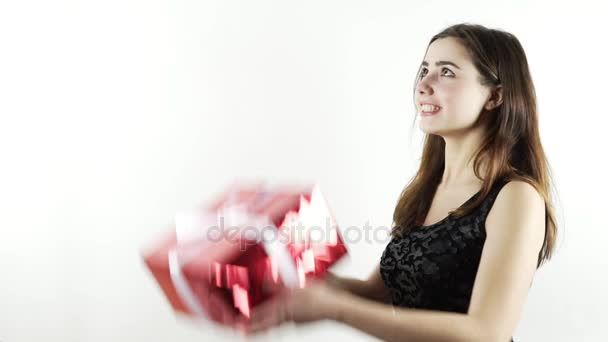 Oldukça neşeli kız atmak bir şekilde dekore edilmiş kırmızı kutusu, ağır çekim vurdu. Doğum günü hediyesi zevk eğlenceli isoated beyaz arka plan, çocuksu, siyah tişörtlü genç kadın var. Neşeli ve samimi duygusal ruh hali — Stok video