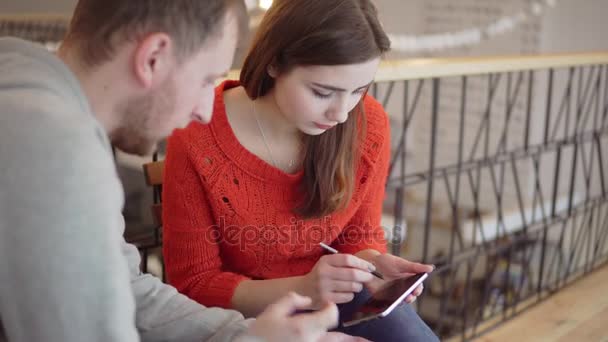 Młoda kobieta siedzi w kawiarni w pobliżu człowieka z smartphone, malowanie na telefon — Wideo stockowe