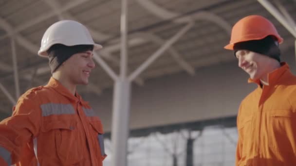 Two construction workers high five. They look very happy. New constructed building with columns at the background — Stock Video