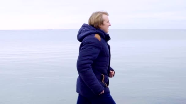 Young man running in beautiful nature landscape by the sea in coat — Stock Video