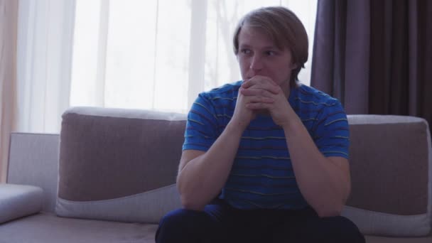 Young man sitting on the sofa at home in the living room waiting for something — Stock Video