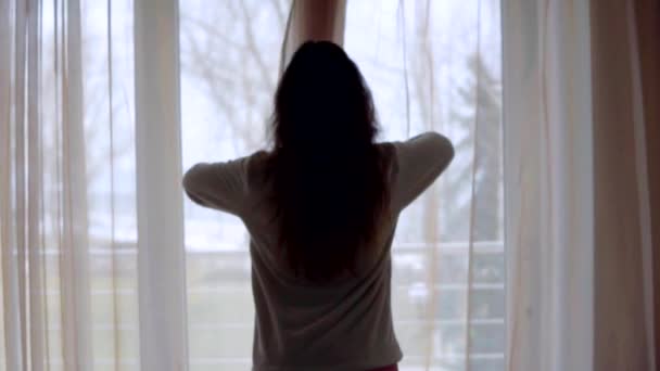 Young woman in sleeping costume opening the curtains in the morning at home — Stock Video