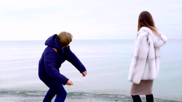 Casal jovem jogando pedras no mar no inverno. Movimento lento — Vídeo de Stock