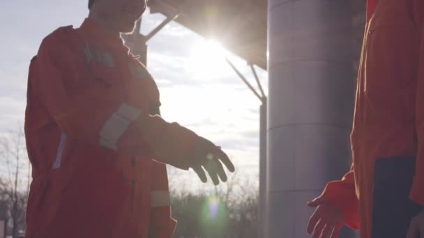 Two construction workers in orange uniform and hardhats shaking hands at the bulding object — Stock Video