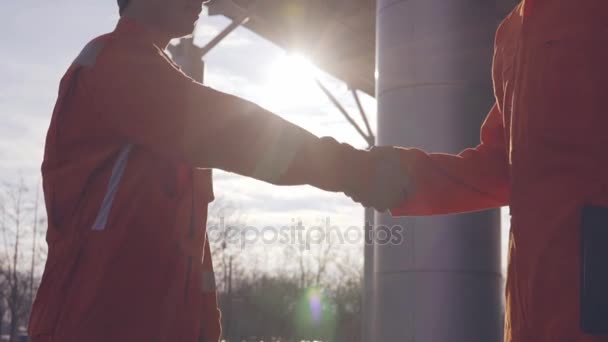 Closeup view of two construction workers in orange uniform and hardhats shaking hands at the bulding object — Stock Video