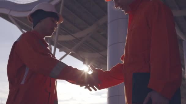 Closeup view of two construction workers in orange uniform and hardhats shaking hands at the bulding object. Slowmotion — Stock Video