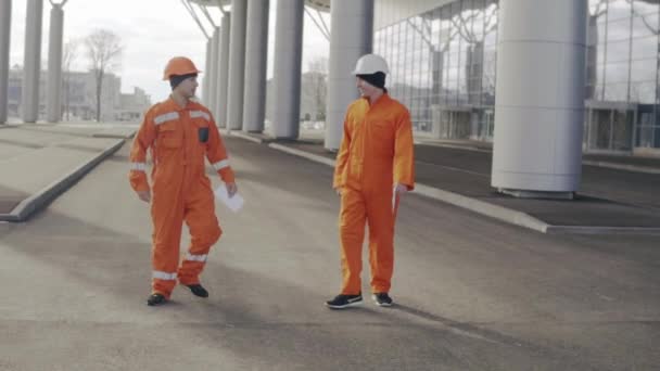 Two construction workers in orange uniform giving high five. They look very happy. New constructed building with columns at the background — Stock Video