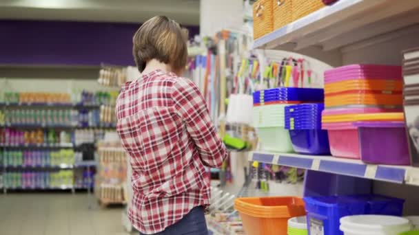 Eine junge Frau im karierten Hemd wählt eine Plastikbox im Einkaufszentrum. 4k — Stockvideo