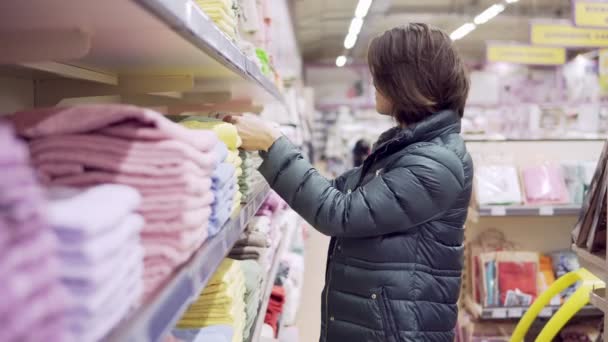Красивая женщина в пальто инспектирование и покупка полотенец в супермаркете — стоковое видео