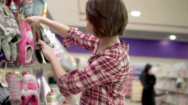 Brünette Frau, die im Supermarkt Pantoffeln wählt. Auswahl bequemer Homewear — Stockvideo