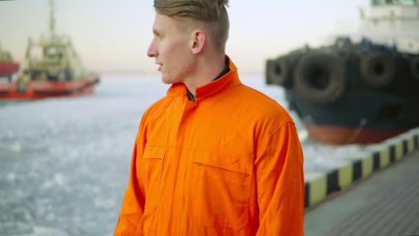 Trabajador portuario en uniforme naranja mirando al mar y disfrutando del paisaje del puerto en invierno. Mar helado — Vídeos de Stock