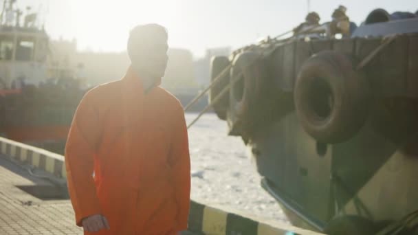 Harbor Worker en uniforme naranja está junto al mar. Lente de bengala. Lento. — Vídeos de Stock