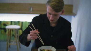 Closeup görünümünü noodle yemek çubukları kullanarak yemek çalışan bir adam. Başarı olmadan yemek çubukları tutmayı öğrenme ve bir çatal alarak.
