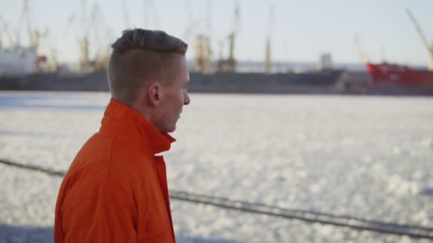 オレンジ色の制服で港湾労働者が海沿い歩いています。スローモーション — ストック動画