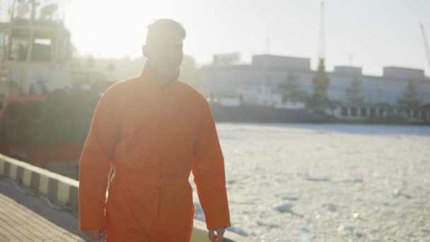 Harbor Worker en uniforme naranja está junto al mar. Lente de bengala. Lento. — Vídeo de stock