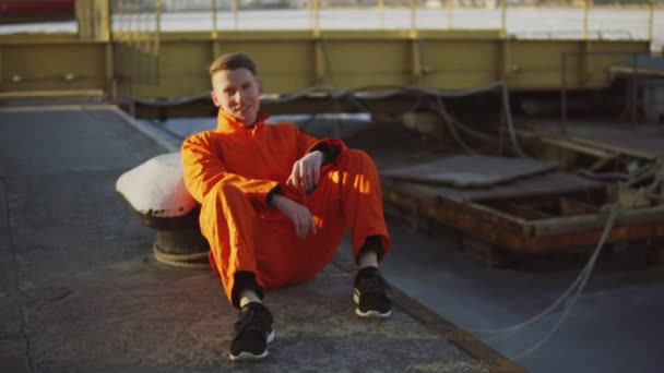 Porträtt av ung arbetstagare i orange uniform sitter under hans paus vid havet — Stockvideo