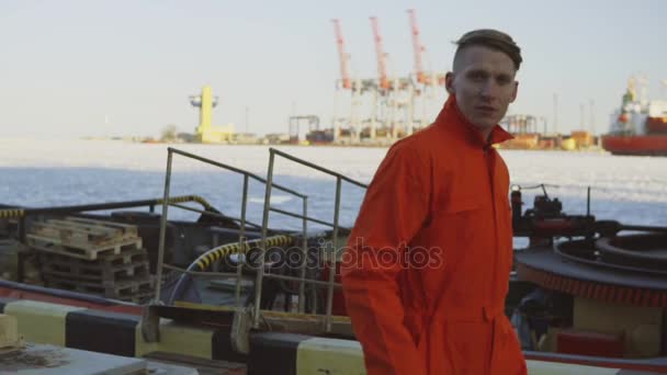 Joven trabajador en uniforme naranja caminando por el puerto junto al mar durante su descanso. Tiempo libre — Vídeos de Stock