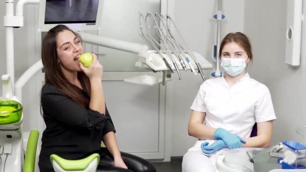 A fogászati irodai lány csípős egy zöld alma ül a fogorvos eljárások után. Egészséges fogak és egészséges mosoly. — Stock videók