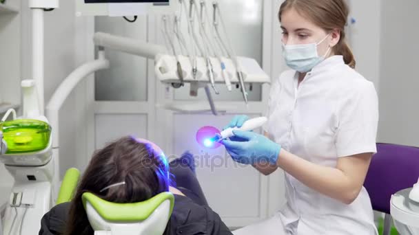 Молодая женщина-стоматолог в маске и перчатках с использованием ультрафиолетового оборудования для полимерной закалки — стоковое видео