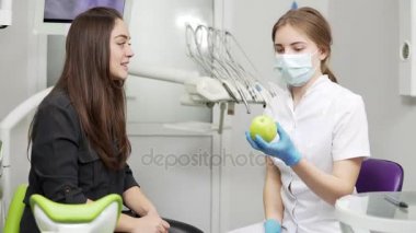 Yeşil elma mutlu ve sağlıklı hasta için yordamlar sonra sunan genç kadın diş hekimi