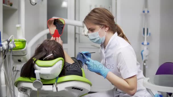口腔医学。年轻的女牙医谈到客户端，给她一面镜子. — 图库视频影像