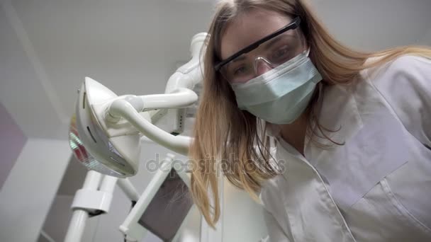 Молодая женщина дантист в маске осматривает пациента с помощью инструментов, стоя на пациенте, глядя в камеру, стоматологи лицо — стоковое видео