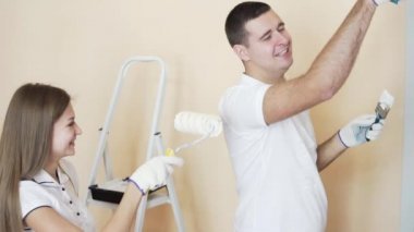 Genç çift beyaz gömlek içinde yeni evlerinin süsleyin. Genç karı koca boya merdaneleri kullanarak duvar boya vardır. Eğleniyor. Kadın onu boyama tişört kocalar