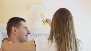 Genç çift beyaz gömlek içinde yeni evlerinin süsleyin. Genç karı koca boya merdaneleri kullanarak duvar boya vardır. Güzel çift onların yeni ev onarım yapma.