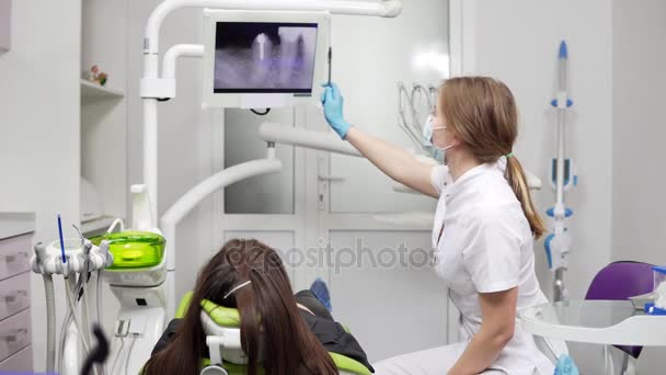 A jovem dentista mostra dentes de raios-X num comprimido na cadeira. Dentista feminina com máscara e jaleco. Dentes saudáveis e saúde dentária . — Vídeo de Stock