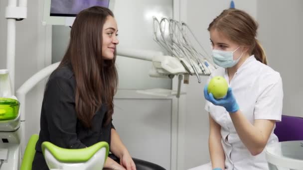 Jovem dentista oferecendo maçã verde para paciente feliz e saudável após os procedimentos — Vídeo de Stock