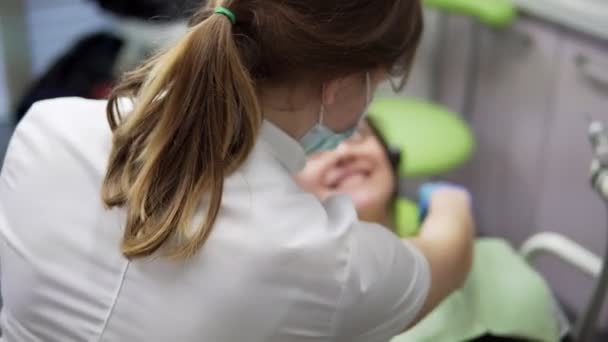 Jovem médica a tomar um guardanapo para a paciente. Higiene oral e atendimento odontológico: Médico dentista que trabalha com paciente na clínica odontológica. Conceito de saúde . — Vídeo de Stock