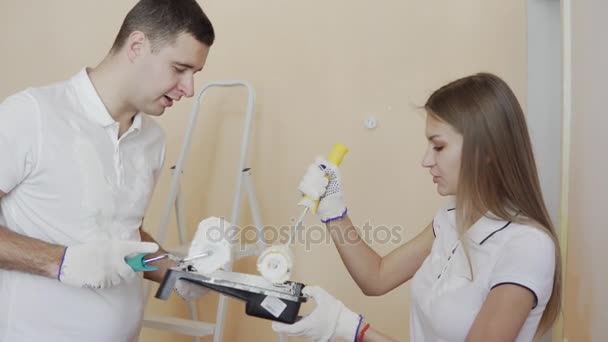 Woman is holding the roller in ready-mix paint. Young couple decorate their new apartment. Young husband and wife are painting the wall. Beautiful couple making repairs in their new flat. — Stock Video