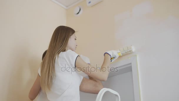 Молодая счастливая пара украшения комнаты - покраска стены с краски ролика и кисти. Женщина и мужчина стоят на лестнице и улыбаются. . — стоковое видео