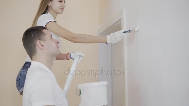 Jonge gelukkige paar versieren kamer - jonge vrouw staande op de ladder en schilderen muur met kwast. — Stockvideo