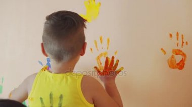 Mutlu anne ve sevimli oğlu birlikte onların renkli el izleri duvara terk eğleniyor. Annesi onu onun el izi yapmak yardımcı olmak için onun güneş kollarına al